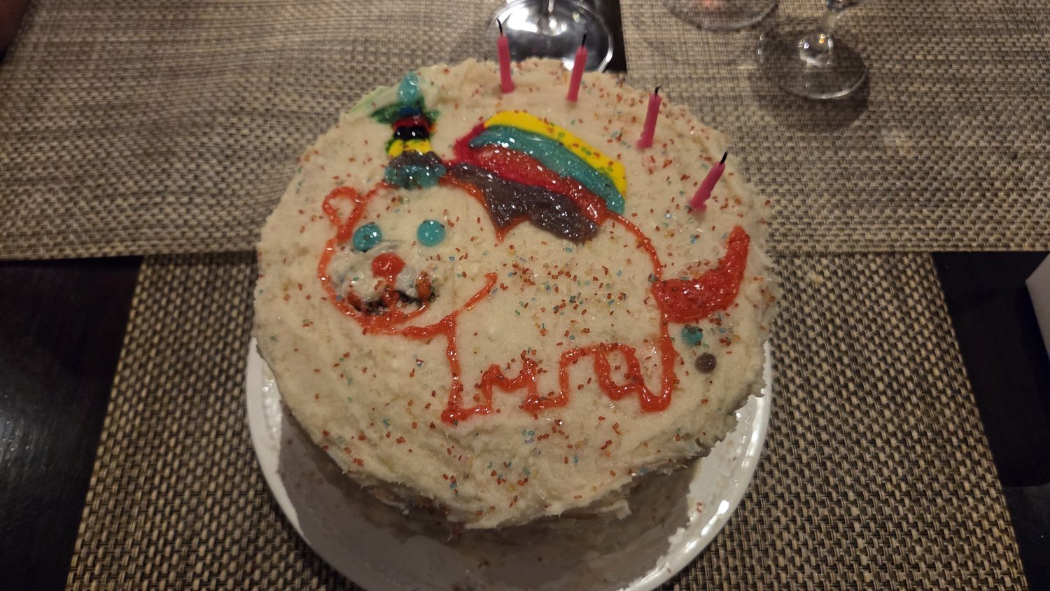 The finished cake: white buttercream on confetti sponge, a wobbly orange piped unicorn, sprinkles, and a sour-belt rainbow arcing up from the animal's rear.